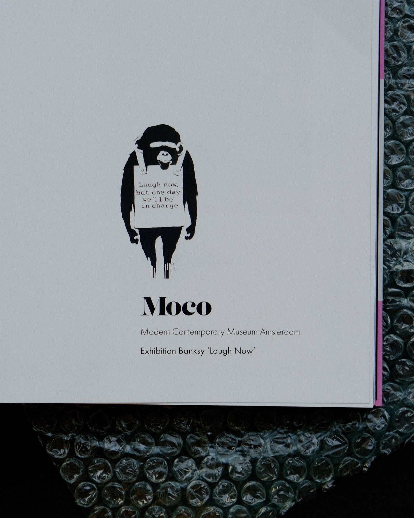 Close-up look at the title page of the Banksy Catalogue Moco where written Moco, Modern Contemporary Museum Amsterdam, Exhibition Banksy 'Laugh Now'.