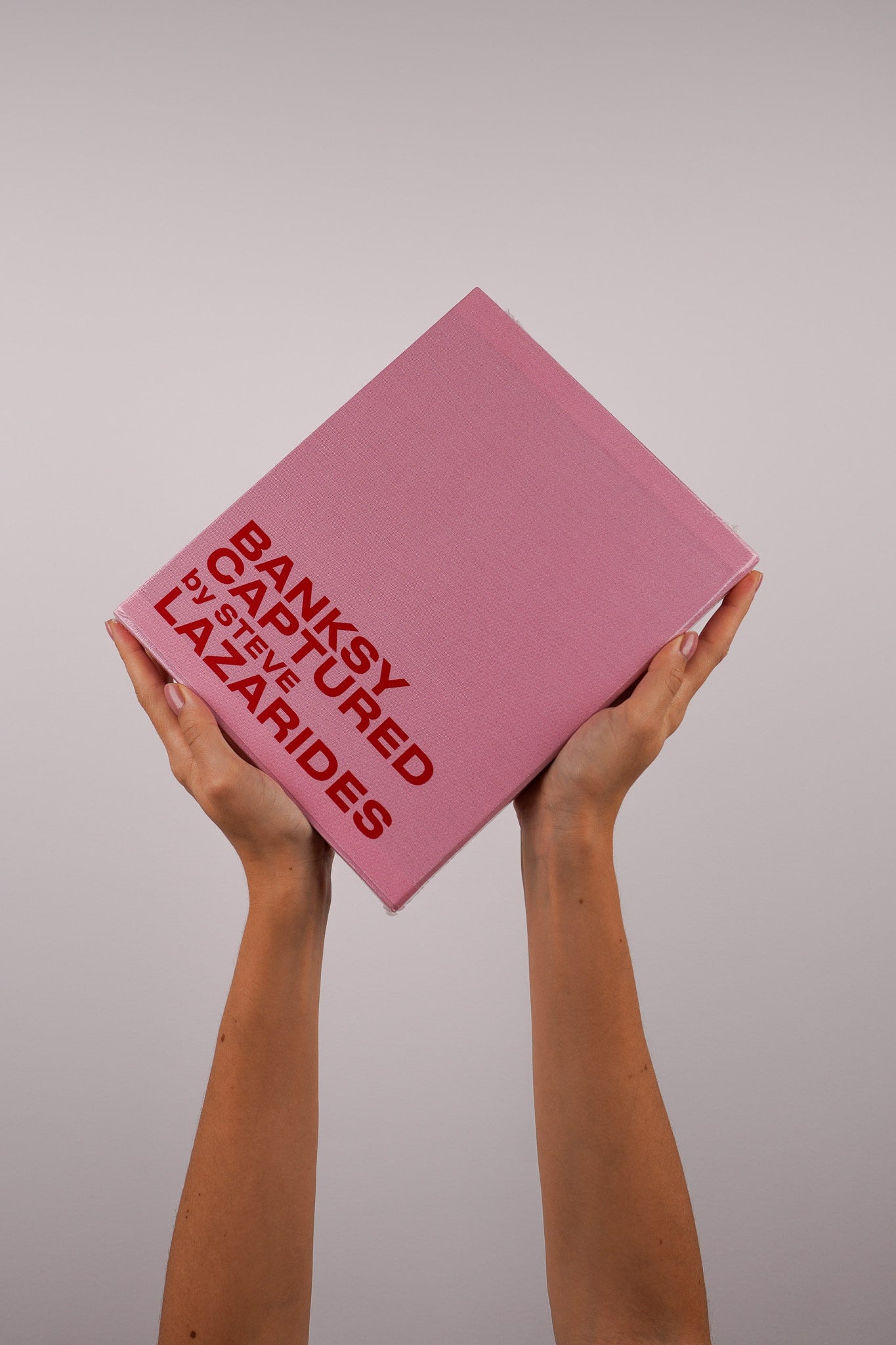 Hardcover edition of Banksy Captured Volume 2 by Steve Lazarides, featuring a pink fabric slipcover with screenprinted text.