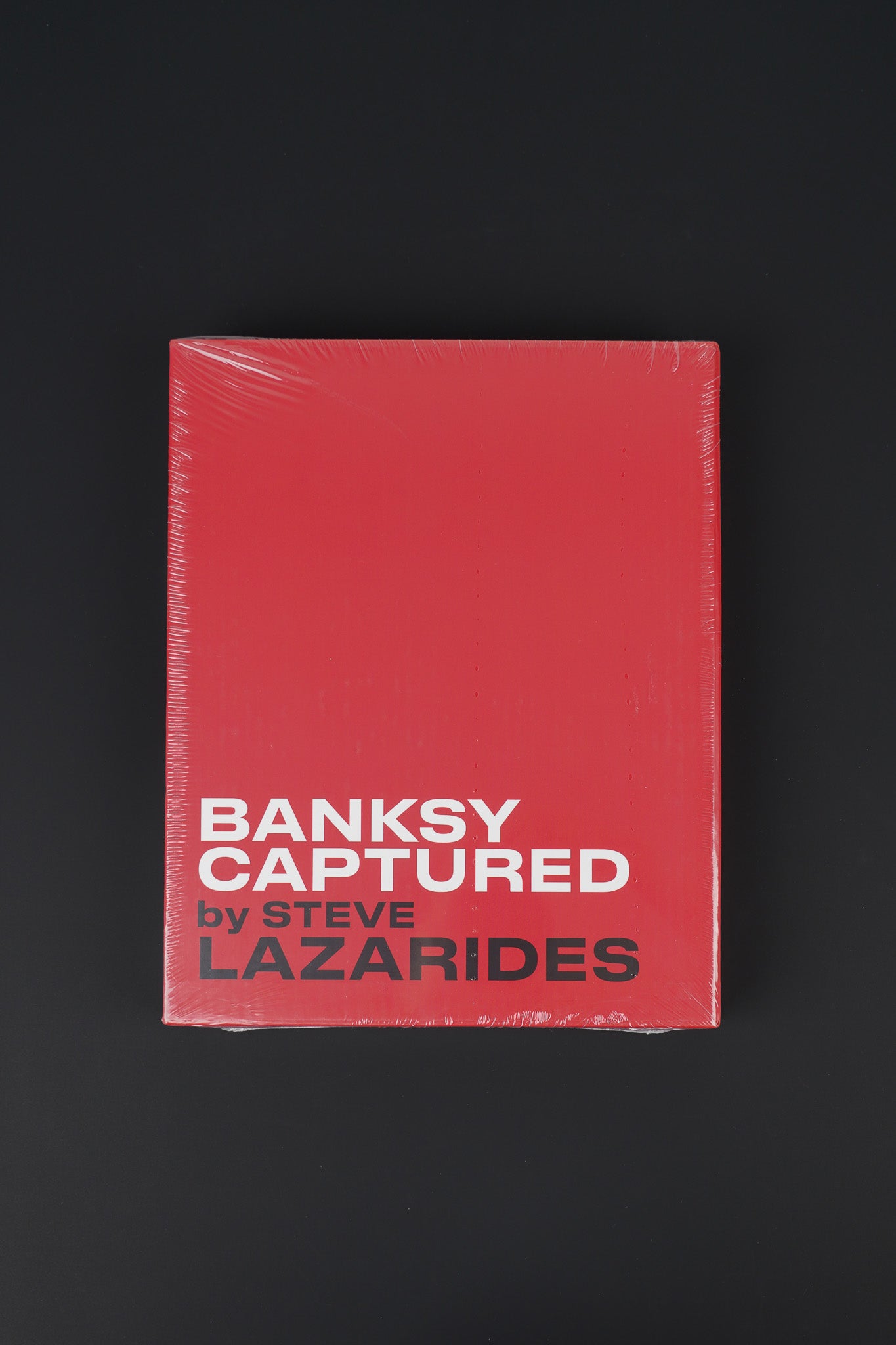 Front view of the sealed Banksy Captured red edition in its slipcase, showcasing the bold design and elegant slipcover.