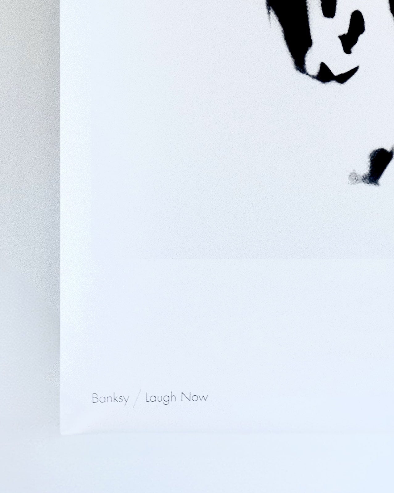 Close-up look of the print of "Laugh Now” by Banksy where written Banksy / Laugh Now.